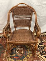 Front view of rattan rocker showing woven seat and back with rounded armrests and curved wood frame.