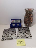 Photo showing Washington Quarters State Collection volumes 1 and 2 books, US Liberty Coins collector set in blue display case including two coins, and a 9.5-inch glass vase filled with pennies and penny rolls