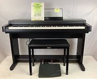 Front view of digital piano on stand with bench, pedal bag and manual on music rest
