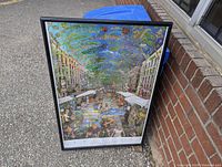 Photo of the framed Barcelona poster leaning outdoors against a wall and blue bin.