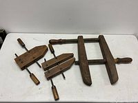 Set of three antique solid wood furniture clamps on a white surface, showing their overall shape and size