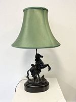 Full front view of the table lamp showing the green fabric lampshade and metal figural sculpture base.