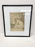 Full view of the framed etching of a seated lady in a black frame with white matte.