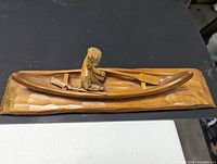 Top angle view of the wood carving showing the seated man paddling inside the canoe on a carved wooden base