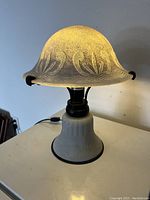 Lit lamp showing warm light through frosted Art Nouveau mushroom-shaped glass shade with organic pattern.