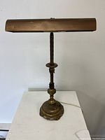 Front view of gilt metal gallery desk lamp with detailed ornamental base and twisted stem.