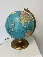 Illuminated terrestrial globe lamp, showing the Americas side with attached power cord and bronze base.