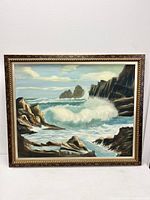 Frontal view of the oil painting showing the seascape with rocky cliffs and waves crashing, framed and signed.