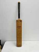 Full view of the old cricket bat showing entire length and handle with wrapped grip.