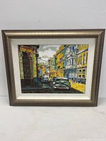 Framed mixed media painting showing colorful Havana street with vintage cars and old buildings, in a silver-toned wood frame and white matte border.