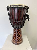 Full front view of the wooden Djabe hand drum showing carved geometric design on the base and rope tension system on drumhead.