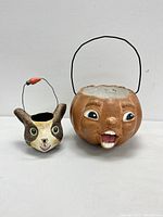 Both vintage papier mache Halloween trick or treat buckets displayed side by side on a white surface showing their front faces and handles.