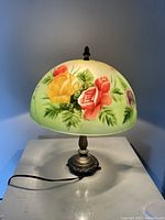 Front view of the reverse painted glass lampshade with red, yellow, and purple floral designs, above antique metal base.