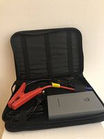 Open black zippered case showing gray 12V jump car starter power bank and black/red jumper cables organized inside.