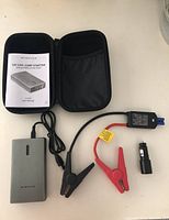 Overview of 12V jump starter kit contents, showing power bank, jumper clamps, adapter, manual inside black zippered case.