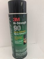 Single image showing the 3M Hi-Strength 90 spray adhesive aerosol can, black with a black cap, with label details visible