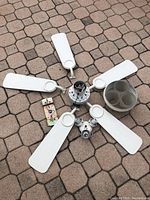Disassembled white ceiling fan with five blades and three-light fixture laid out on a patio surface.