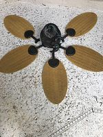 Disassembled gold and black ceiling fan with five woven-style blades and black central housing laid on a granite surface.