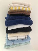 Stack of 14 towels in various colors including blue, white, black, cream, brown, yellow and patterns.