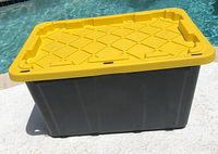 Full view of HDX black and yellow 27-gallon tough tote storage container outdoors on light surface