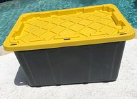 Photo of the HDX 27 gallon tough tote showing the black base and yellow lid with diamond pattern design, placed on ground outdoors.