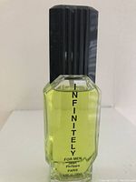 Clear glass cologne bottle with black ridged cap containing yellow liquid. Label shows Infinitely For Men by Jean Philippe Paris.