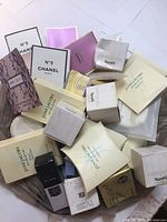 Various ladies perfume, soap, and shower cap samples displayed in assorted small boxes and sachets from brands including Chanel, Juicy Couture, Gucci, Harrods, Elizabeth Arden.