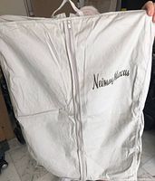 Full view of white cloth zippered garment case with Neiman Marcus printed on front, held upright showing zippered closure.