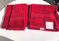 Three red velour towels (2 bath towels and 1 hand towel) arranged folded on a white surface, showing their texture and vibrant red color.