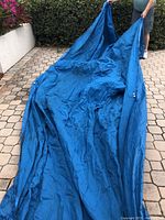 Image of large royal blue boat cover being held up by a person outdoors, showing size and fabric texture.