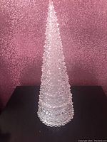 Full view of the tall sparkling Christmas tree centerpiece with clear crystal-like texture, cone shape, and detailed texture that resembles cut crystal or acrylic, displayed against a glittery pink background.