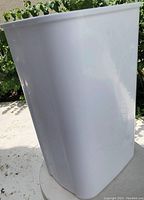 Side view of the tall white plastic waste basket showing smooth, plain surface and slightly tapered shape.