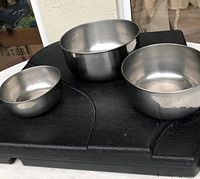 Photo showing three stainless steel mixing bowls of different sizes arranged on a black surface, highlighting their shape, finish, and condition.