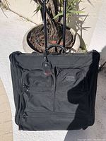 Front exterior of black TUMI rolling suitcase with telescoping handle and dual front zippered compartments.