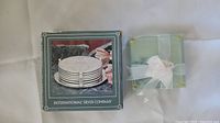 Boxed set of International Silver Company metal coasters and tied glass coasters shown from above on white surface.
