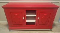 Front view of red and white entertainment stand showing two closed doors and two center shelves with knobs.