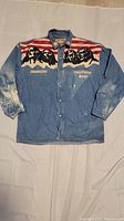 Front view of the blue denim jean shirt with graphic print on chest and button closure.