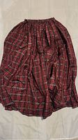 Full view of a red and black plaid fabric dress or skirt laid flat showing elastic waistband and gathered fabric