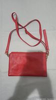 Front side view of a small red shoulder bag laid flat showing the adjustable strap and zipper.