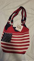 Front view of the shoulder bag showing the knitted American flag design with red and white stripes and blue with white stars corner.
