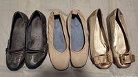 Photo of three pairs of women's shoes size 10: black Skechers flats, beige Naturalizer flats, and metallic gold Bandolino flats
