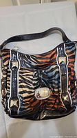 Front view of the Kathy Van Zeeland colorful animal print bag with black patent leather accents and silver hardware.