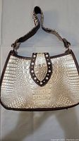 Front view of brown and beige faux leather handbag showing crocodile pattern and studded strap