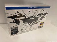 Packaging of The Dark Knight Trilogy Blu-ray Ultimate Collector's Edition in sealed box showing shattered bat logo and edition details.