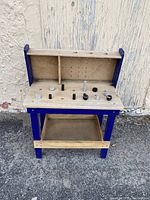 Children's wooden workbench painted blue and natural wood, showing pegboard back and pegs on top surface and lower shelf.