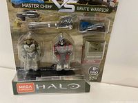 Front view of boxed Mega Construx Halo figure set showing Master Chief and Brute Warrior figures with included weapons and display bases in packaging.