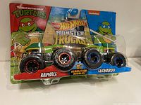 Front view of two Hot Wheels Monster Trucks in package featuring Teenage Mutant Ninja Turtles characters Raphael and Leonardo. Packaging includes colorful TMNT backing cards and blister pack.