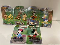 Front view of the six Hot Wheels cars in original packaging branded with Disney characters Pluto, Chip, Goofy, Donald Duck, Minnie Mouse, and Mickey Mouse.