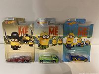 Three Hot Wheels Despicable Me diecast cars in original packaging laid out side by side
