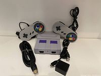 Mini Super Nintendo console with two wired controllers, USB power adapter, and HDMI cable arranged on white surface.
